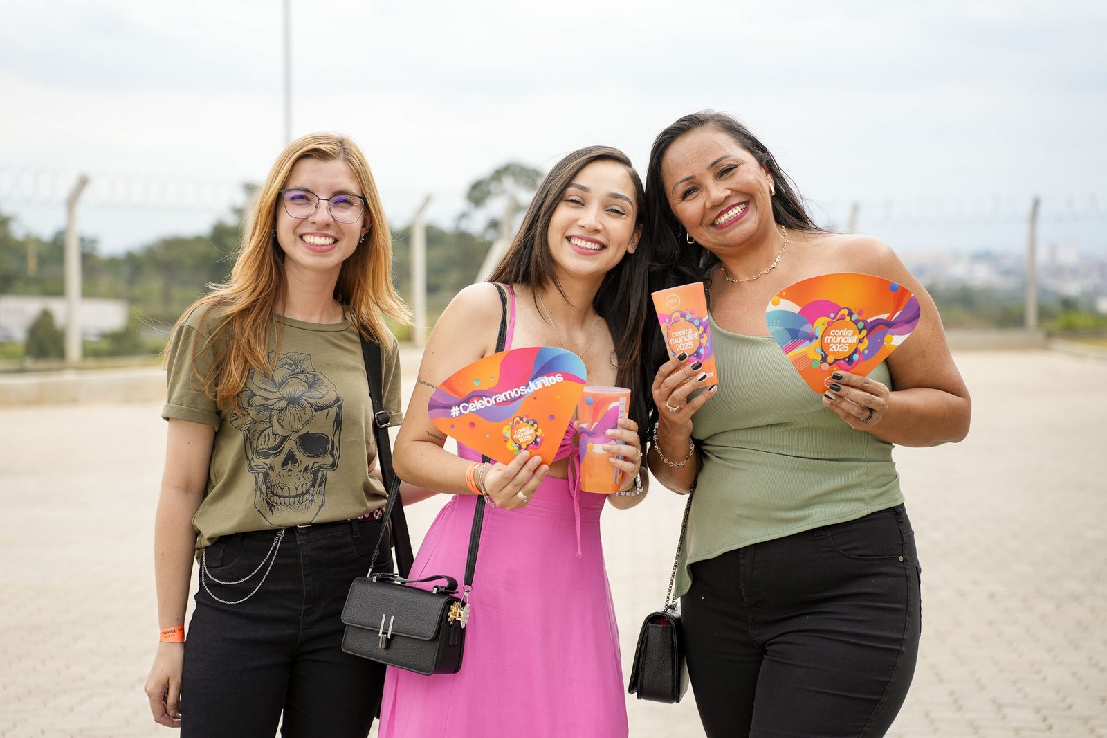 Três convidadas sorrindo ao ar livre com leques do evento